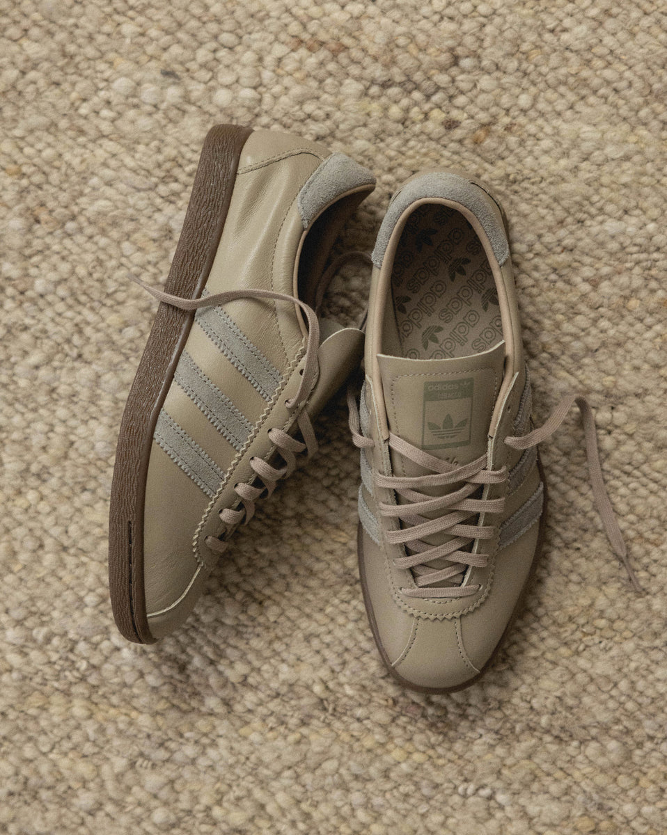 adidas tobacco grey Introducing the Shoes, blending rustic tones with vintage charm. The monochromatic design, highlighted by serrated 3-Stripes, pairs effortlessly with any outfit. Crafted with premium pigskin, these trainers offer both luxury forward finesse. adidas Originals TOBACCO JOURNAL STANDARD